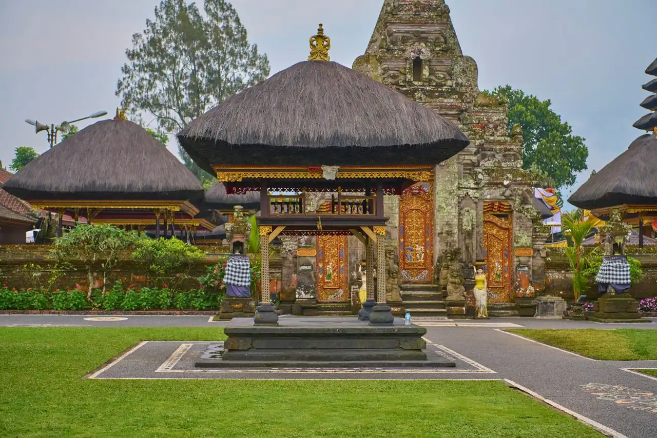 A close-up view of the stone steps leading up to the main gateway at Pura Saraswati temple. The staircase is flanked by detailed, moss-covered stone carvings of mythical dragon-like creatures (Naga) acting as guardians, with a large stone demonic guardian statue standing further up near the golden door.