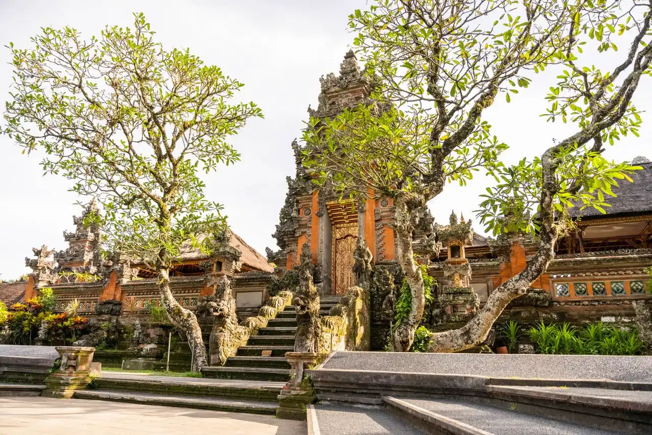 Low-angle view of stone stairs leading up to a grand split gateway inside the inner courtyard of Taman Ayun Temple Mengwi Bali, surrounded by frangipani trees.
